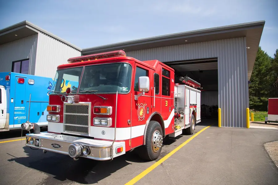 Red fire truck and blue emergency response vehicle parked outside a station under a clear sky.