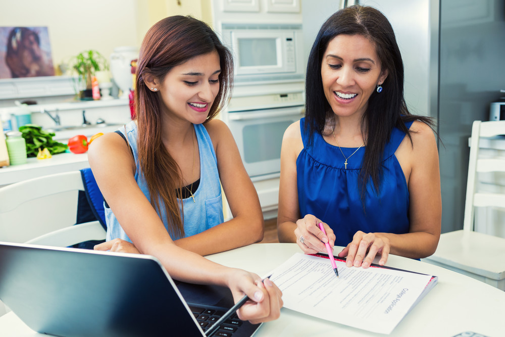 Mother and daughter sitting at kitchen table reviewing homework