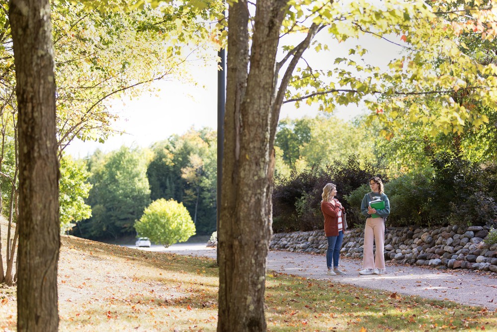 two female students standing on path holding books and talking