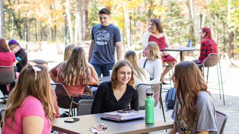 group of students sitting outside on lakeside patio talking and studying