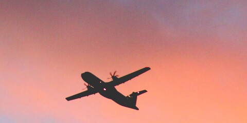 A silhouette of a plane against a pink and purple sky.