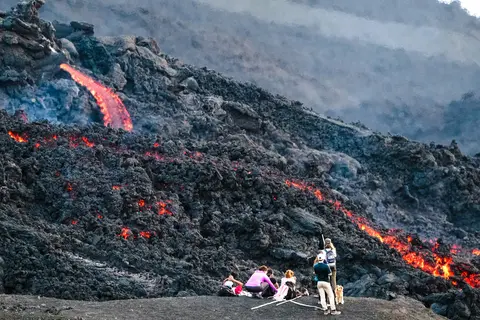 People watching volcanic lava flow on a dark rocky landscape.