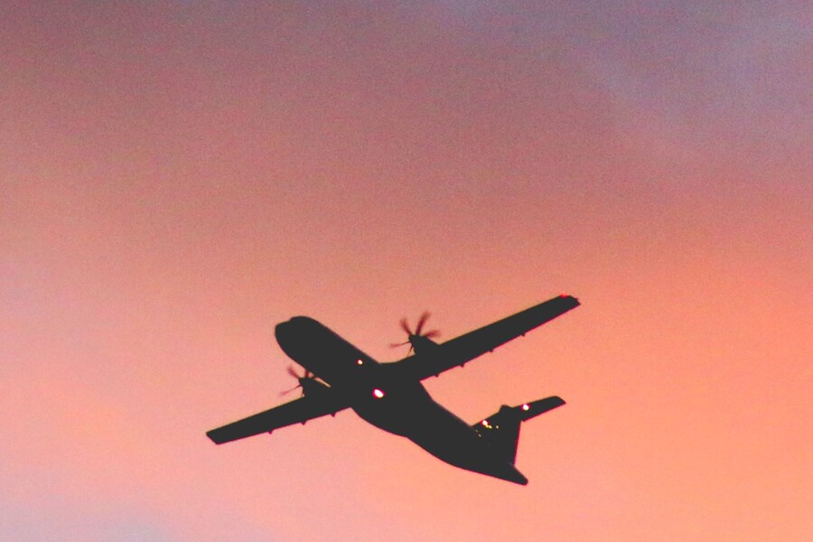 A silhouette of a plane against a pink and purple sky.